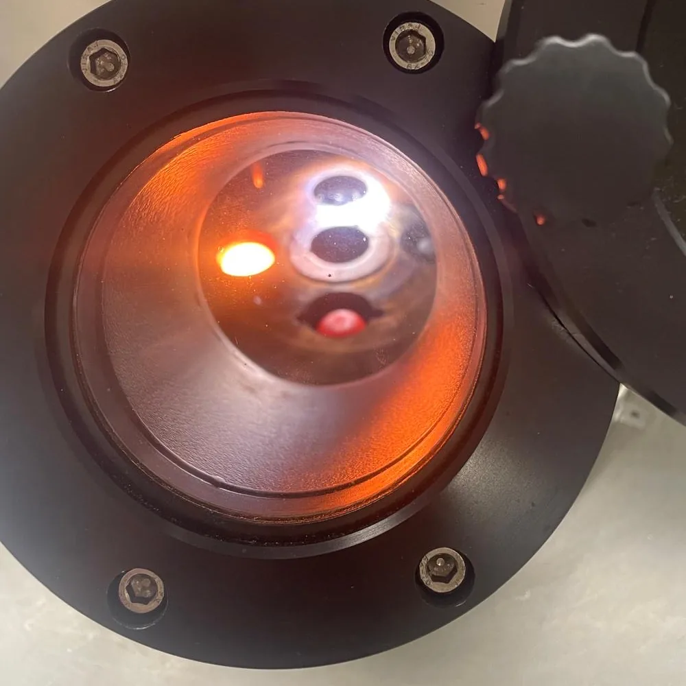 An alloy button glowing orange inside the arc-melting furnace, seen through the viewport